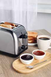Photo of Toaster with roasted bread, coffee and jams on wooden table