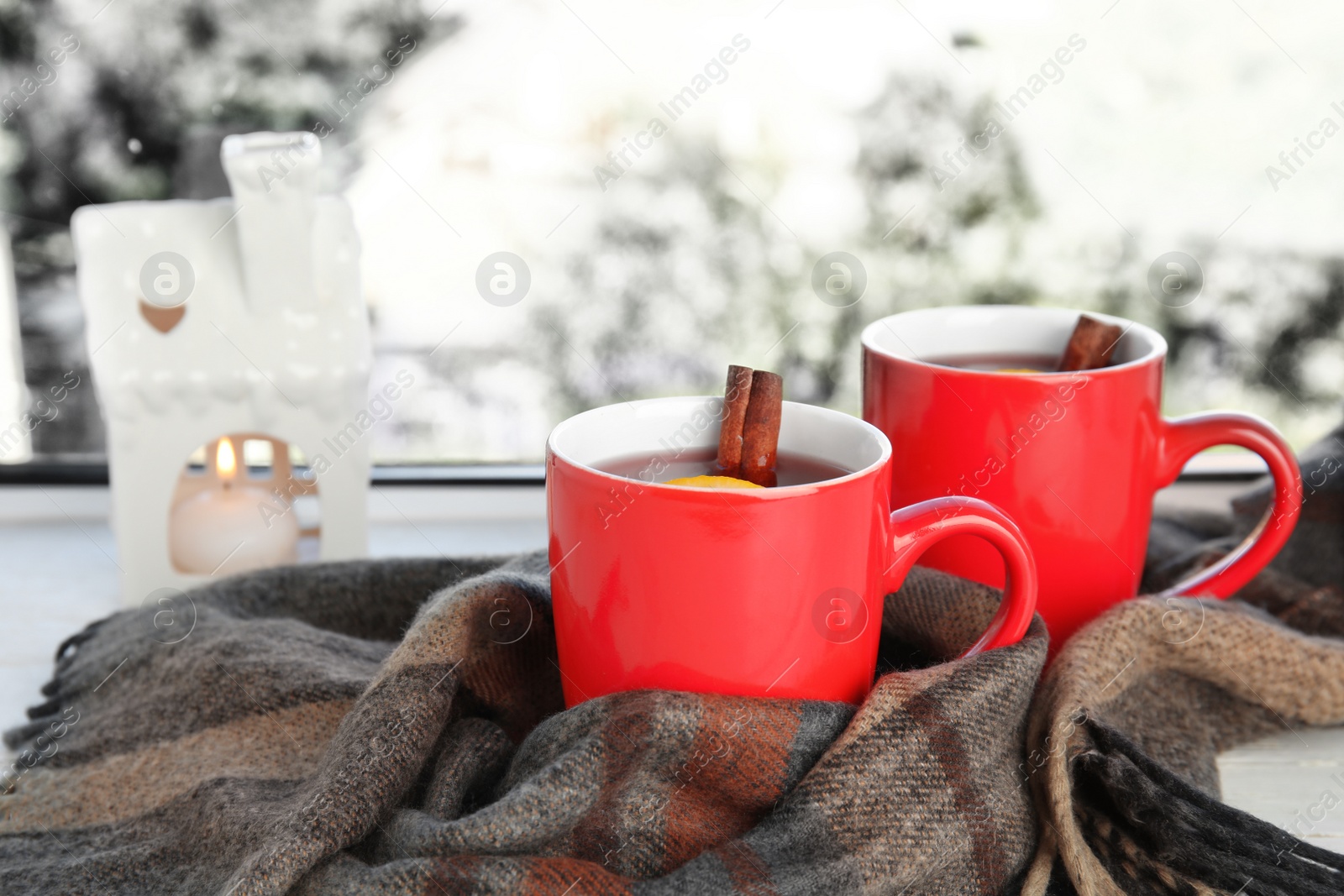 Photo of Cups of hot winter drink with scarf on window sill indoors