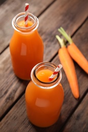 Photo of Freshly made carrot juice in bottles on wooden table