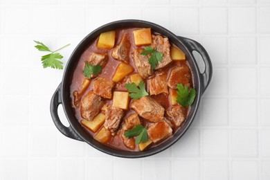 Delicious goulash in pot on white tiled table, top view
