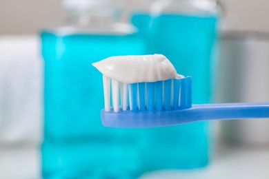 Toothbrush with paste near mouthwash on blurred background, closeup