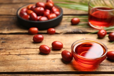 Photo of Palm oil in glass bowl, tropical leaf and fruits on wooden table. Space for text