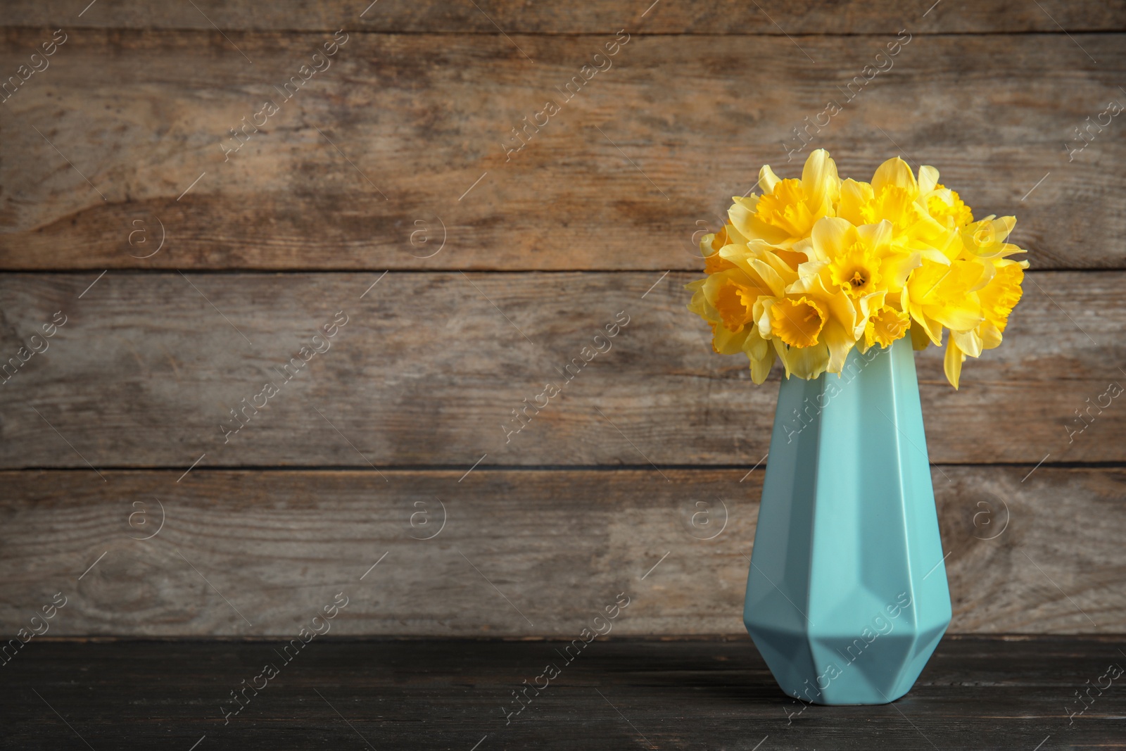 Photo of Bouquet of daffodils in vase on table against wooden background, space for text. Fresh spring flowers