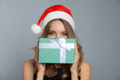 Photo of Happy young woman wearing Santa hat with Christmas gift on grey background