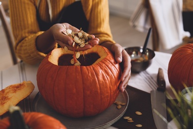 Photo of Woman making pumpkin jack o'lantern at table, closeup. Halloween celebration