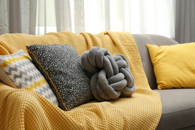 Photo of Soft pillows and yellow plaid on sofa in living room