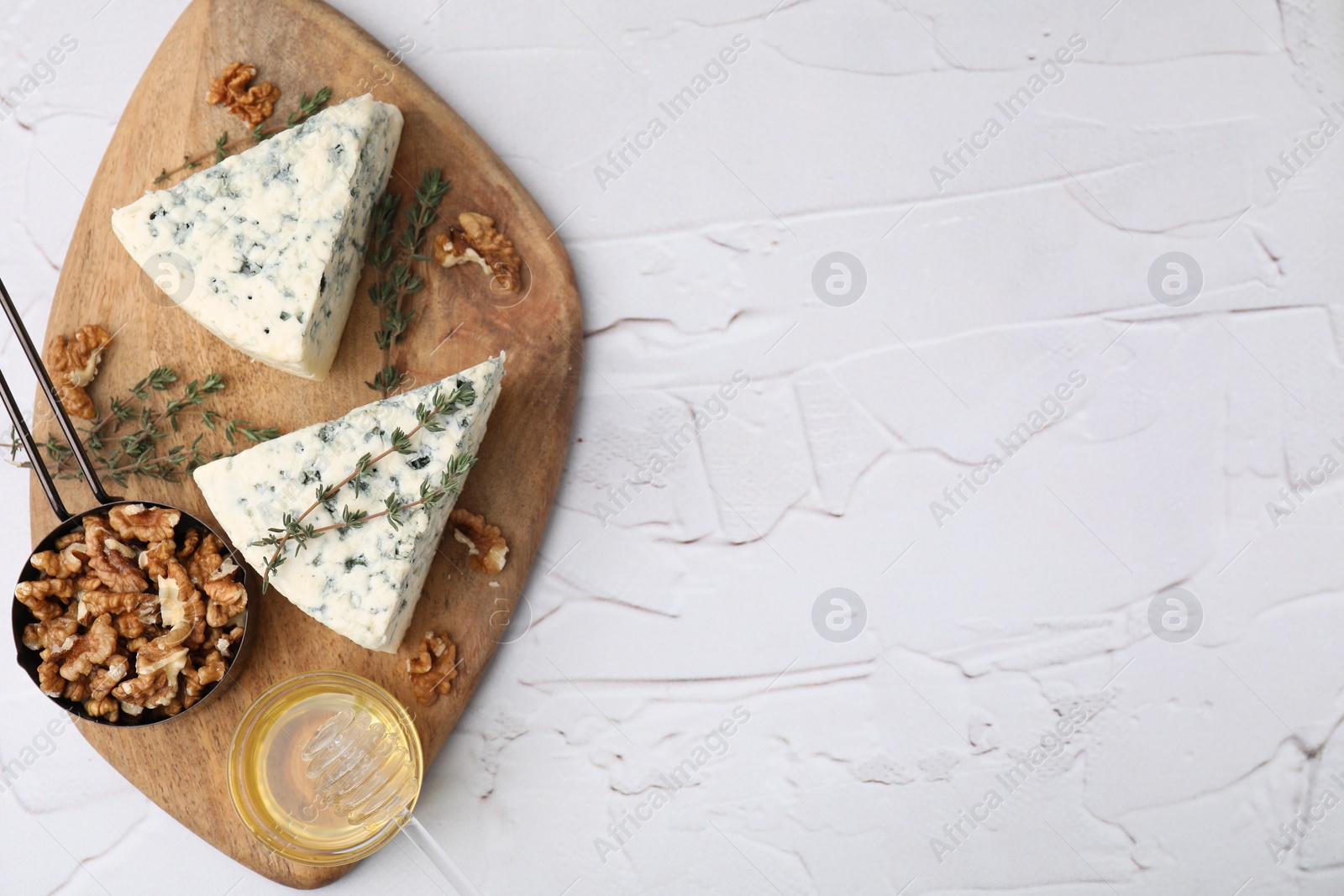 Photo of Tasty blue cheese with thyme, honey and walnuts on white textured table, top view. Space for text