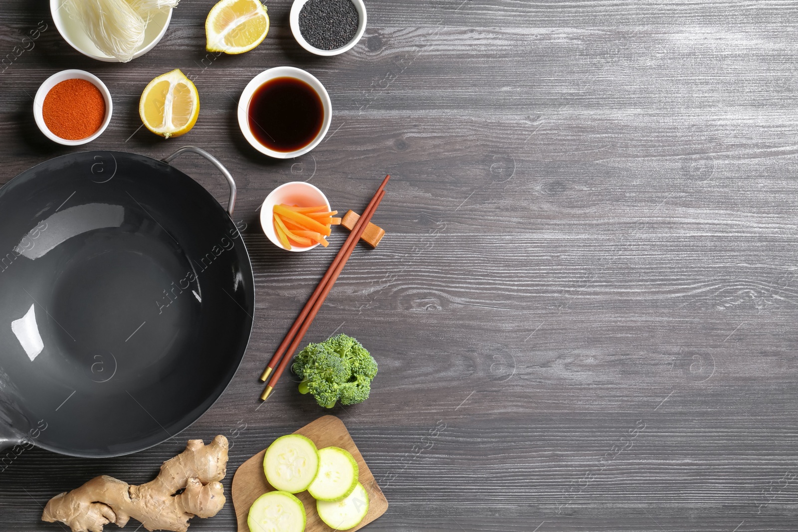 Photo of Empty iron wok, chopsticks and ingredients on grey wooden table, flat lay. Space for text