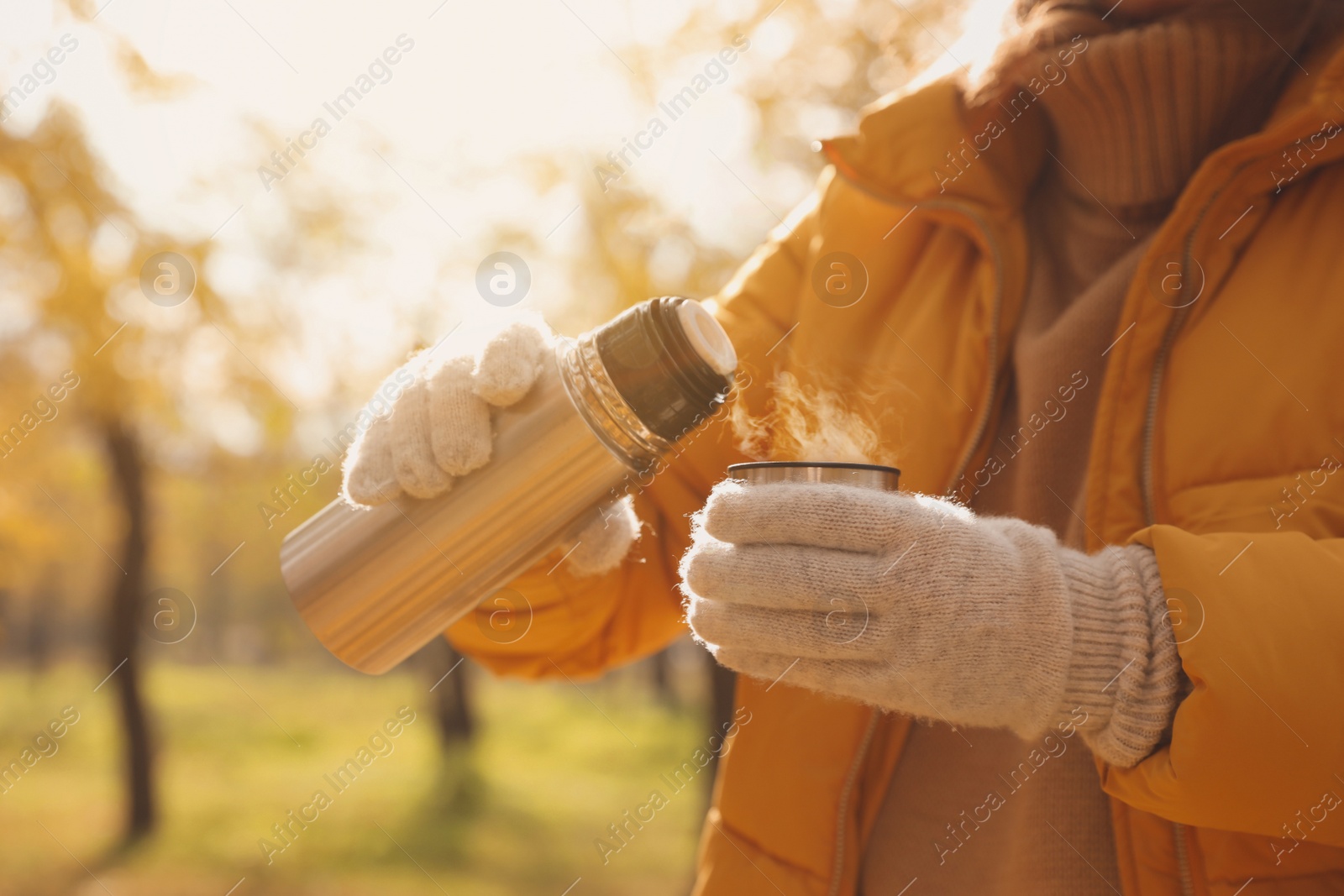 Photo of Woman pouring drink from thermos into cap outdoors, closeup