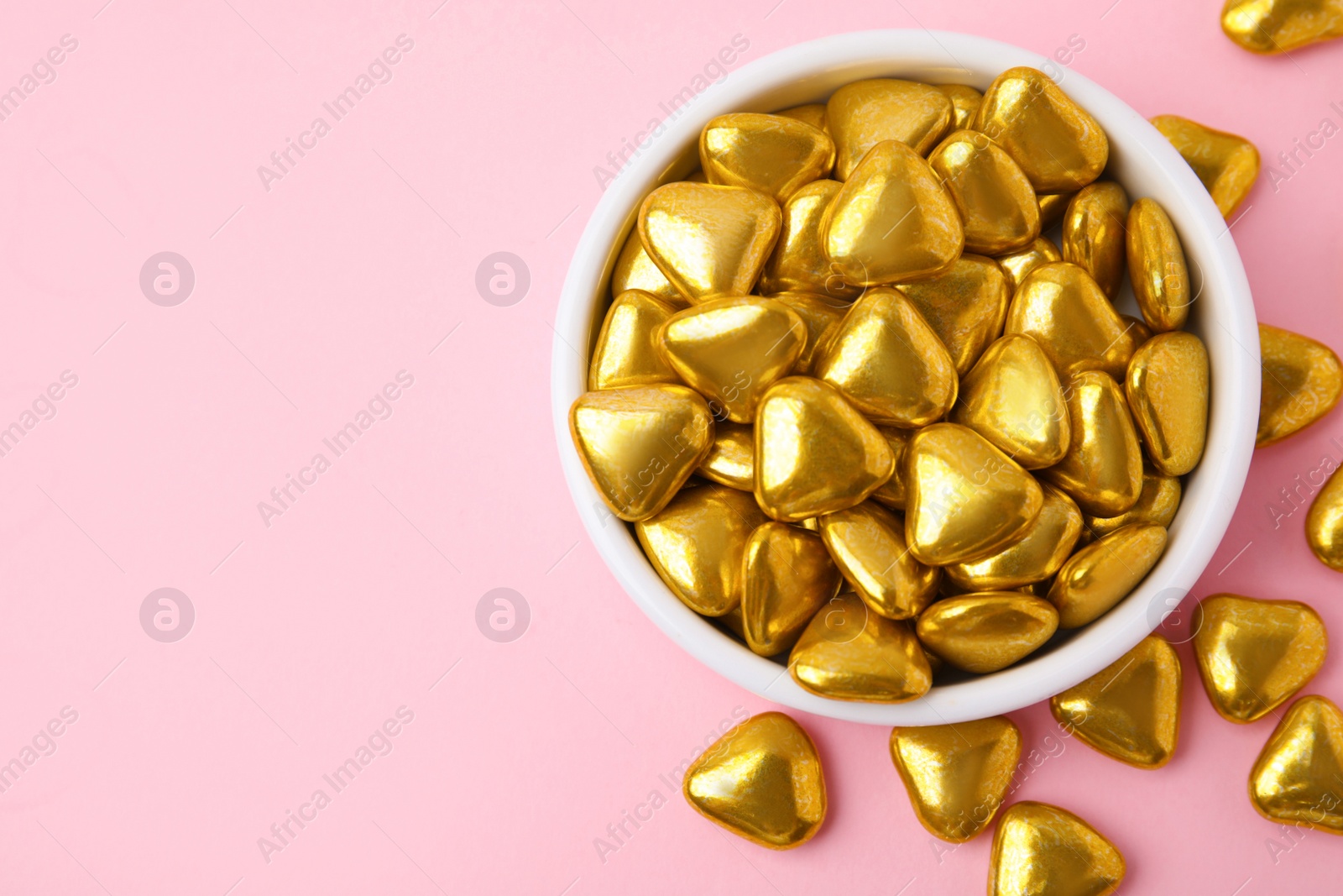 Photo of Bowl and delicious heart shaped candies on pink background, flat lay. Space for text