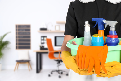 Image of Young chambermaid holding plastic basin with detergents in office, closeup. Space for text