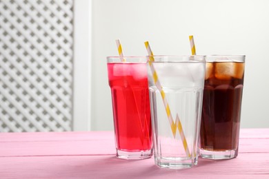 Photo of Glasses of different refreshing soda water with ice cubes and straws on pink wooden table, space for text