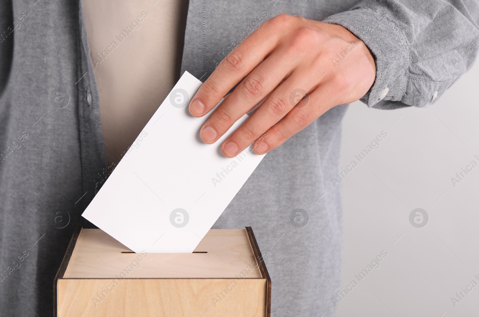 Photo of Man putting his vote into ballot box on light grey background, closeup