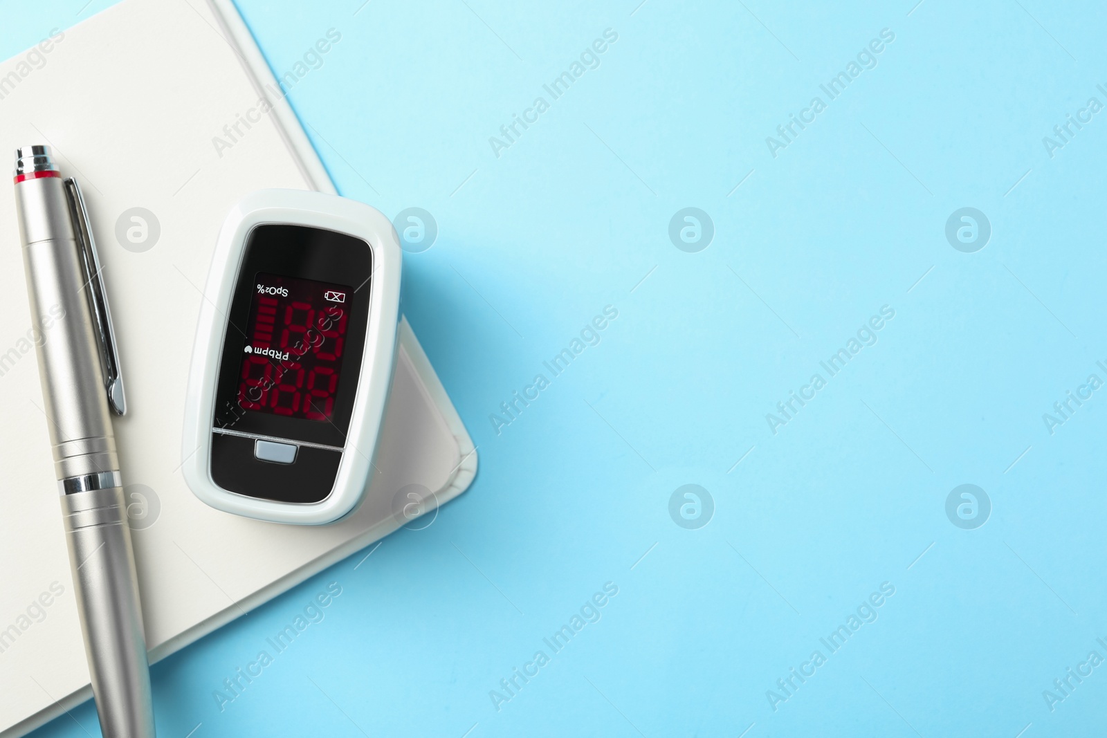 Photo of Modern fingertip pulse oximeter, pen and open notebook on light blue background, flat lay. Space for text