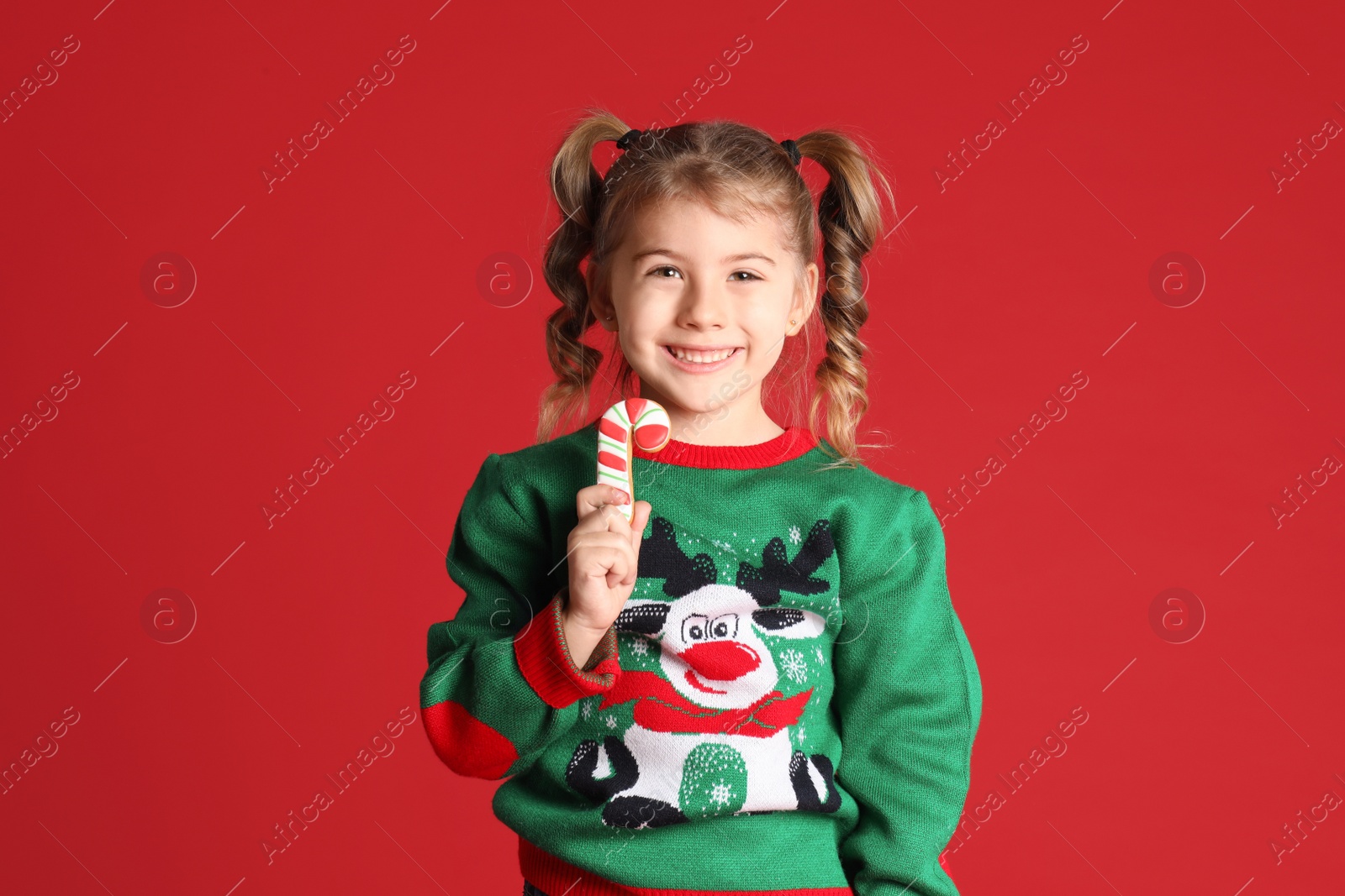 Photo of Cute little girl with Christmas gingerbread cookie on red background