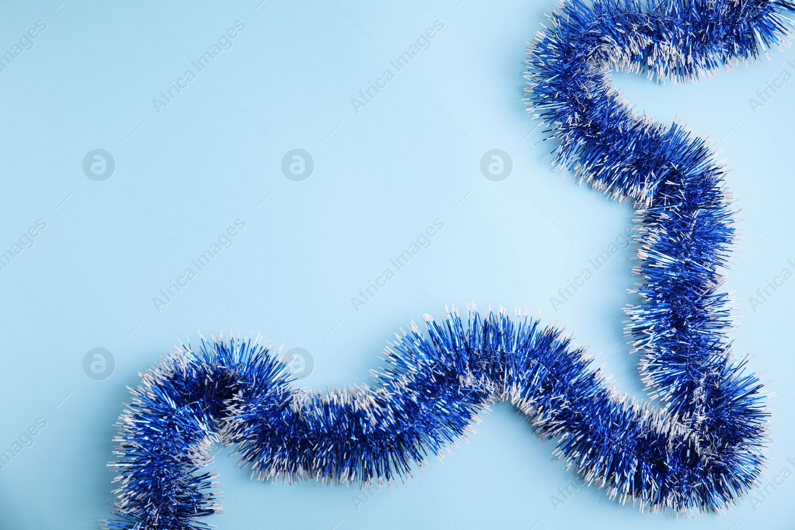 Photo of Bright tinsel on light blue background, top view. Space for text