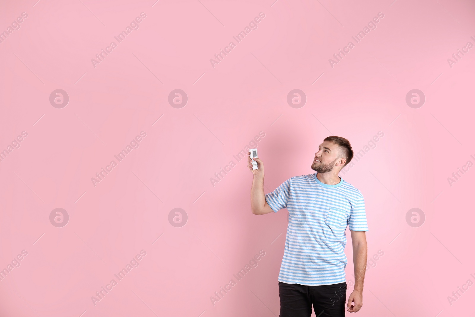 Photo of Young man with air conditioner remote on color background, copy space text