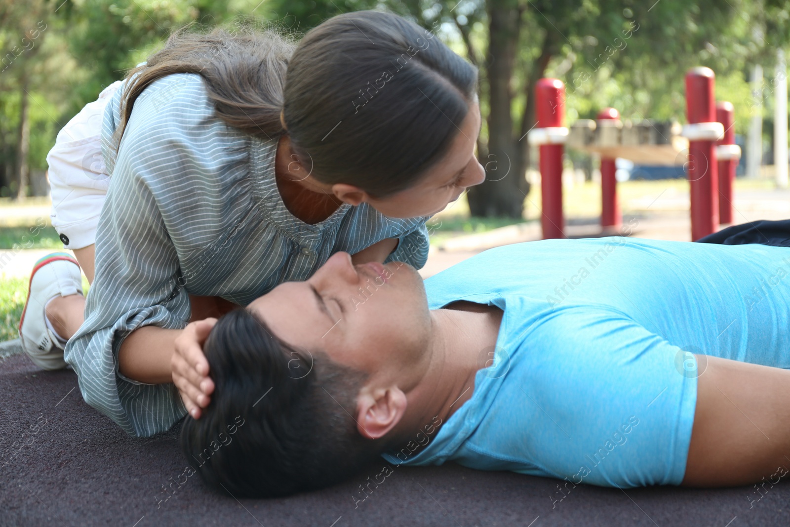 Photo of Young woman checking for breathing of unconscious man outdoors