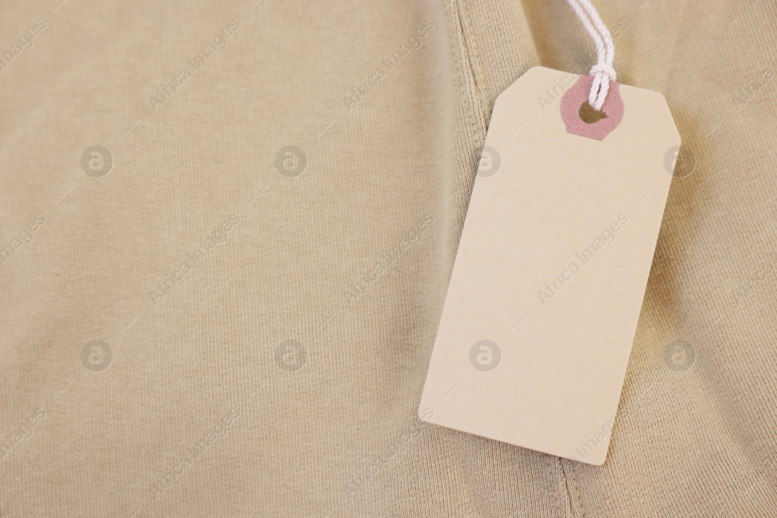 Photo of Cardboard tag on beige garment, top view. Space for text