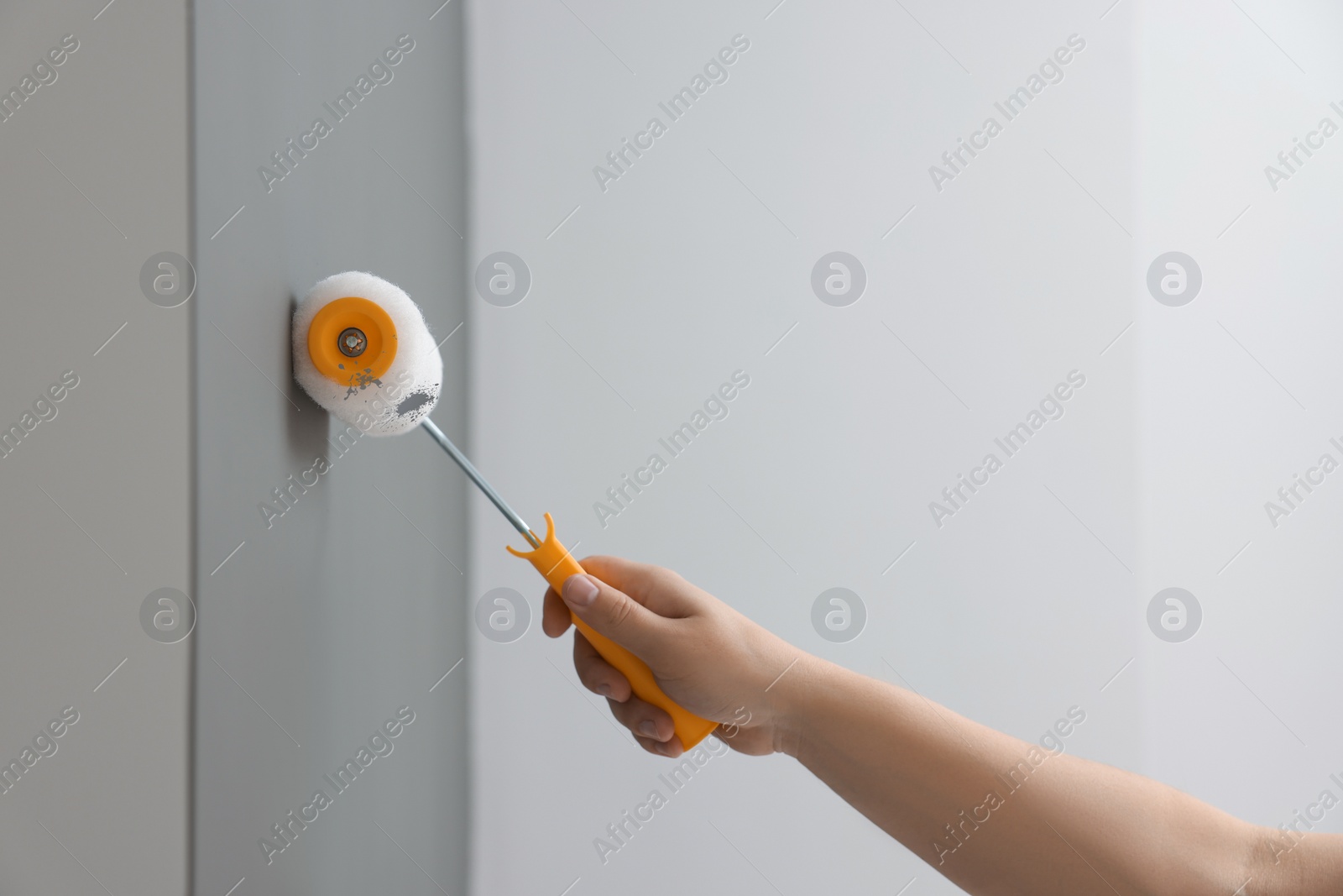 Photo of Worker using roller to paint wall with grey dye indoors, closeup