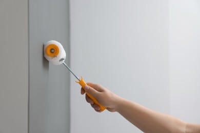 Worker using roller to paint wall with grey dye indoors, closeup