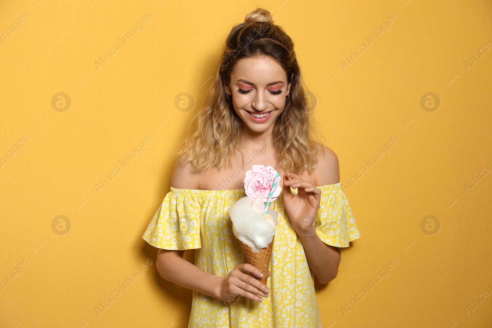 Photo of Portrait of young woman holding cotton candy dessert on yellow background