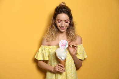 Portrait of young woman holding cotton candy dessert on yellow background