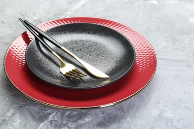 Photo of Clean plates and cutlery on gray textured table, closeup