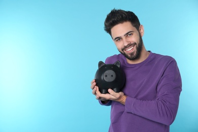 Photo of Happy young man with piggy bank and space for text on color background. Money saving