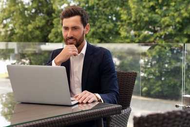 Photo of Handsome bearded man working on laptop in cafe outdoors