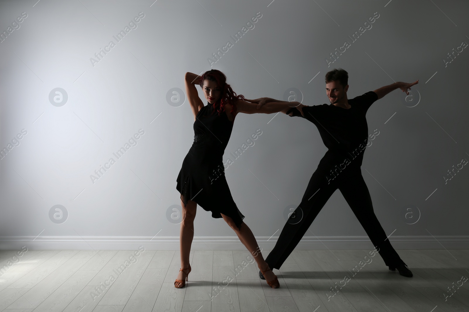 Photo of Beautiful young couple dancing near light wall