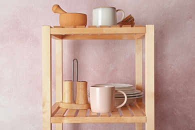 Wooden shelving unit with set of kitchenware near color wall