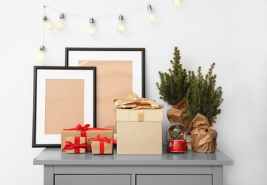 Empty frames, Christmas gifts, evergreen trees and accessories on grey chest of drawers indoors