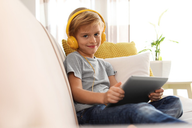 Photo of Cute little boy with headphones and tablet listening to audiobook at home