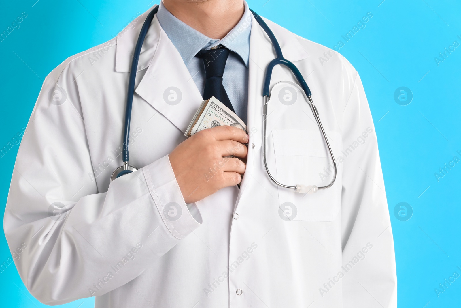 Photo of Doctor putting bribe into pocket on light blue background, closeup. Corruption in medicine