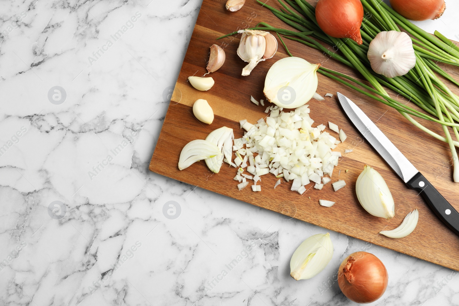 Photo of Board with cut onion and garlic on marble table, top view. Space for text