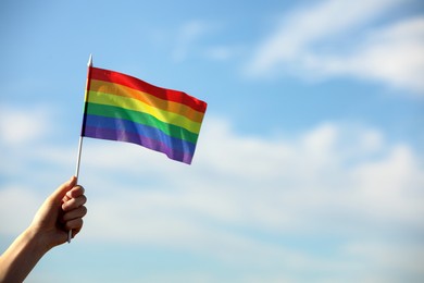 Photo of Woman holding bright LGBT flag against blue sky, closeup. Space for text