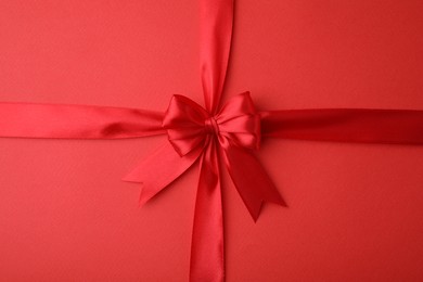 Photo of Bright satin ribbon with bow on red background, top view
