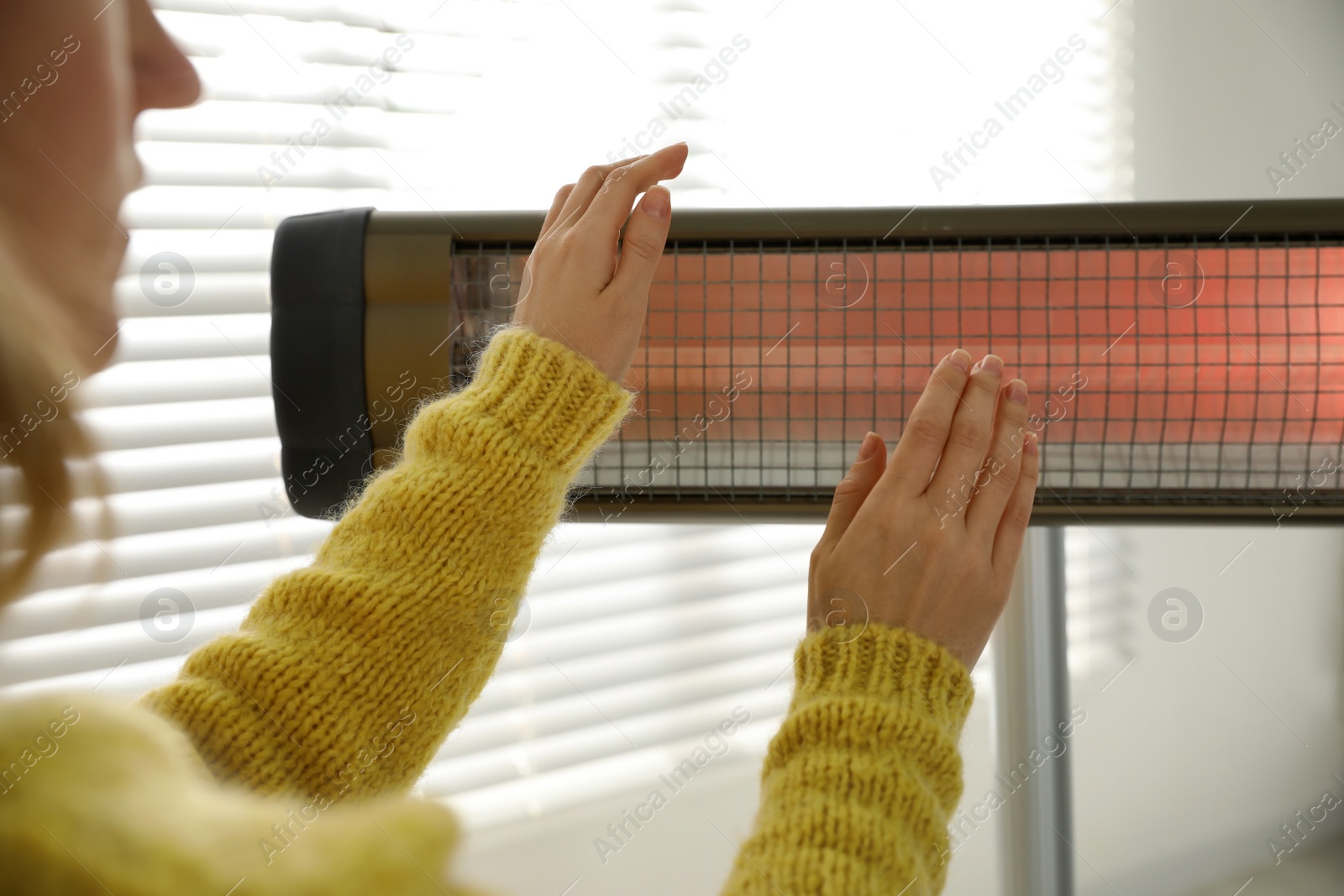 Photo of Woman warming hands near electric infrared heater indoors, closeup