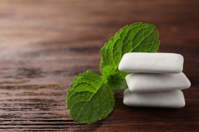 Photo of Tasty white chewing gums and mint leaves on wooden table, closeup. Space for text