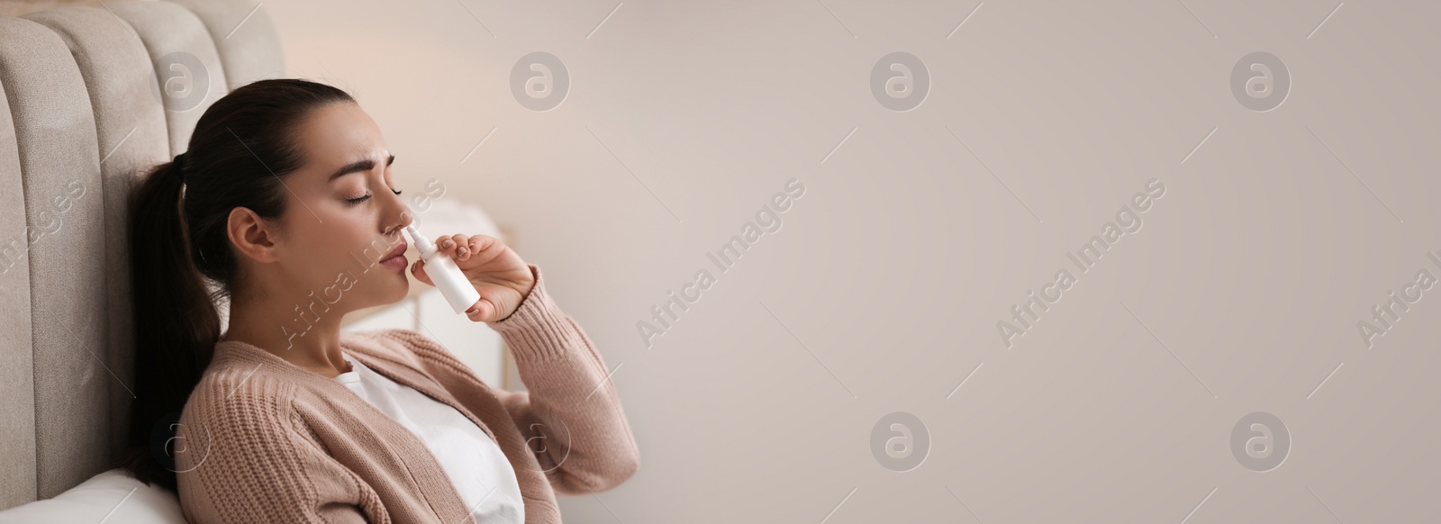 Photo of Sick young woman using nasal spray in bed at home