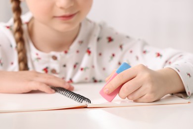 Photo of Girl using eraser at white desk, closeup
