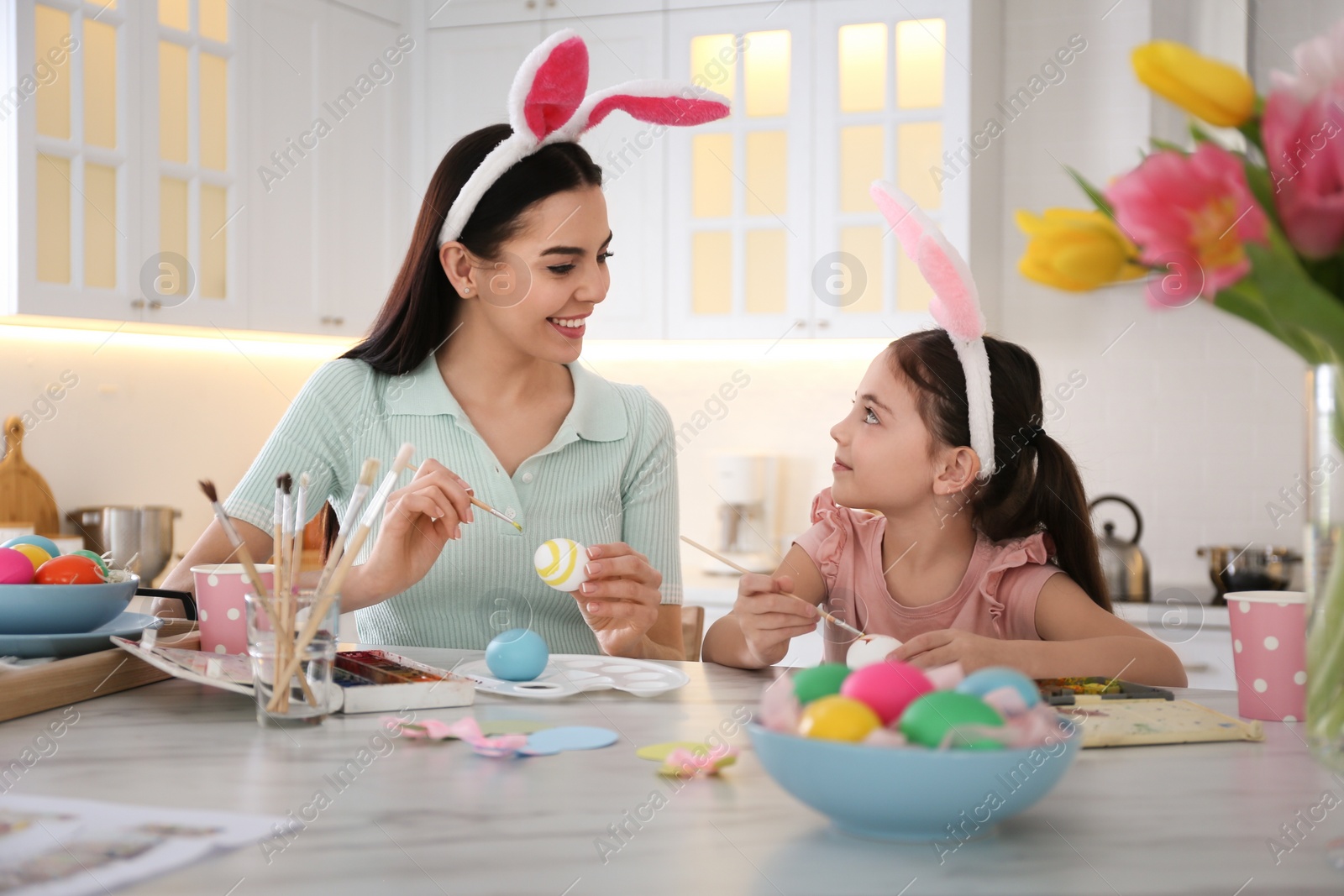 Photo of Happy mother with her cute daughter painting Easter eggs at table in kitchen