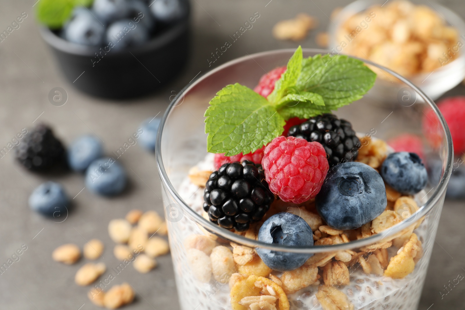 Photo of Delicious chia pudding with berries, granola and mint in glass on table, closeup