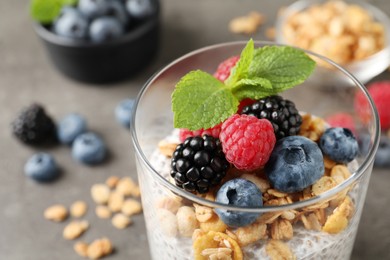 Photo of Delicious chia pudding with berries, granola and mint in glass on table, closeup