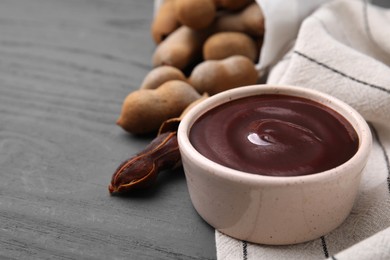 Photo of Bowl of tamarind sauce and fresh pods on grey wooden table. Space for text