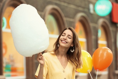 Photo of Happy young woman with cotton candy outdoors