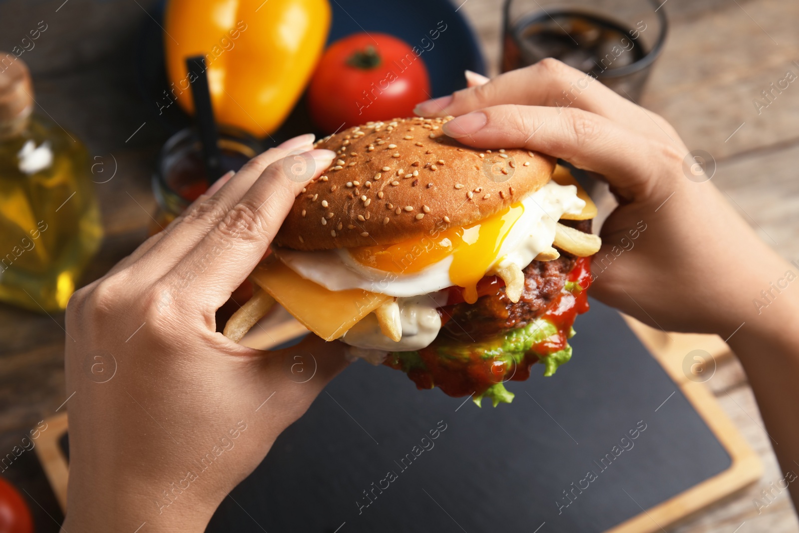 Photo of Woman holding tasty burger with fried egg over table, closeup