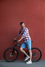 Handsome man with modern bicycle near red wall outdoors