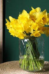 Beautiful daffodils in vase on wicker table against green background